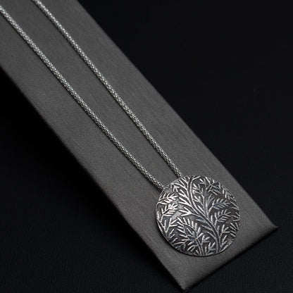 Close up view of handmade sterling silver necklace with round pendant featuring etched wild vine botanical design, oxidized finish on a delicate chain.