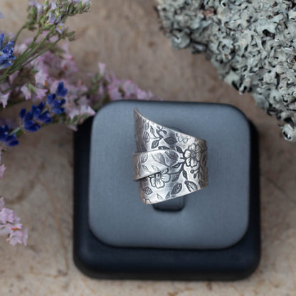 Adjustable sterling silver floral wrap ring by Divella Designs, size 6 3/4 with wildflower texture and patina finish, handmade in Vermont and shown with lichen and dried flowers