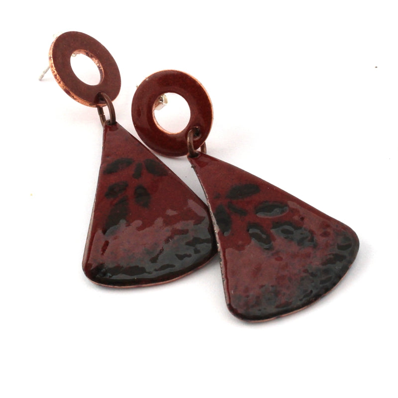 Close-up of oxblood red and black enamel dangle earrings with organic impressed texture and moody botanical-inspired pattern.