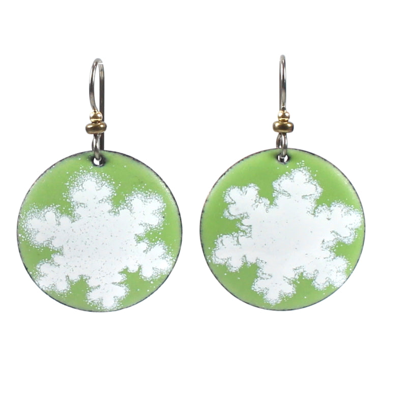 The image shows a pair of green and white snowflake-patterned enamel earrings with metallic accents on the hooks.