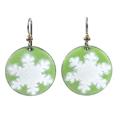 The image shows a pair of green and white snowflake-patterned enamel earrings with metallic accents on the hooks.