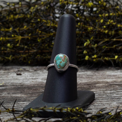 Size 8 King's Manassa turquoise  ring on a dark gray surface with wildflowers in the background