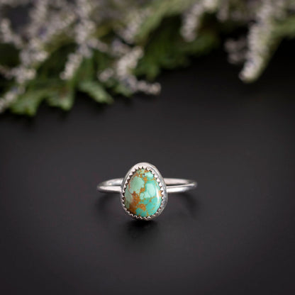 Size 8 King's Manassa turquoise  ring on a dark gray surface with wildflowers in the background
