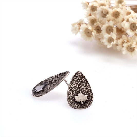Sterling silver teardrop stud earrings with textured finish and small maple leaf detail, ⅞ inch long