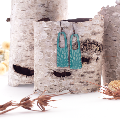 Teal blue handmade enamel earrings with floral pattern and open rectangle design on copper, oxidized ear wires.