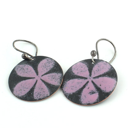 Round dangle earrings featuring a matte black background with a soft pink five-petal floral design, hanging from oxidized metal ear wires on a white background.