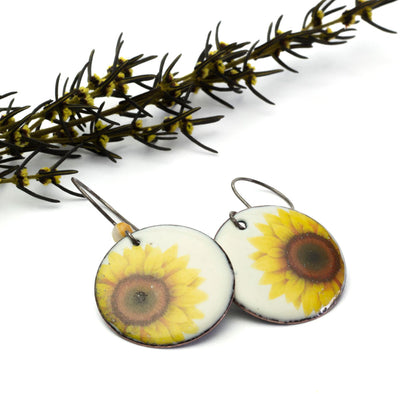 A pair of earrings with a sunflower design, featuring yellow and black colors, made with copper and crazy lace agate gemstones, displayed against a natural background.