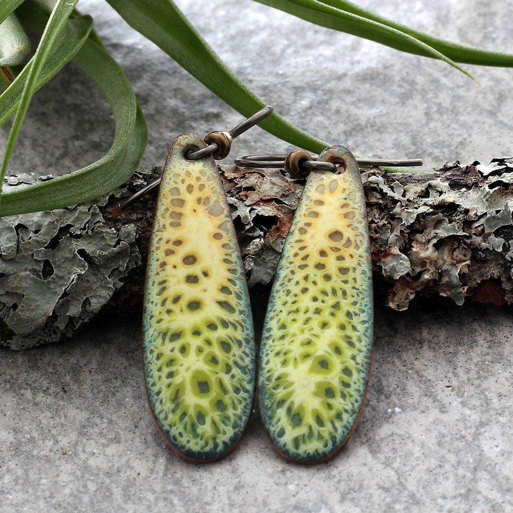 Close-up of yellow and green kiln-fired enamel teardrop earrings with organic mottled texture.